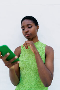 Pensive African American woman student thinking about banking message or investment graph on smartphone screen, looking down with undecided emotion