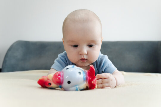 Baby boy lying on bed and gripping teething ring with both hands. Child chewing toy for teething relief. Exploring textures while soothing sore gums. Sensory discovery at home 