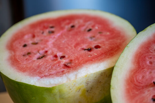 seeded watermelon (Citrullus lanatus) split in half, revealing bright pinkish-red flesh, dark seeds, and a thick green and white rind.