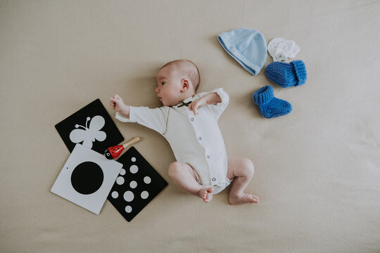 Cute 1 month baby boy lying among various playful colorful toys on beige blanket. Newborn surrounded by vivid objects participating actively in sensory exploration and learning. 