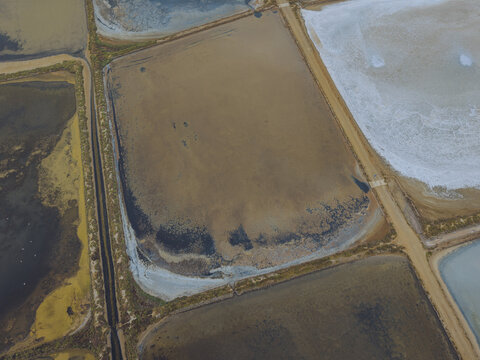 Aerial view of the salt pans at Le Salin de l'ile Saint-Martin de Gruissan, featuring geometric evaporation ponds with varying water colors and earthen dikes in Gruissan, Occitanie, France.