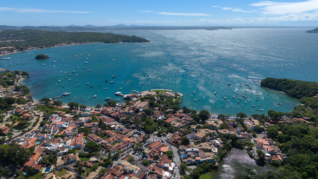 Aerial view of Praia da Armacao and Praia dos Ossos featuring the coastal town with terracotta rooftops, numerous boats anchored in the bay in Armacao dos Buzios, Rio de Janeiro, Brazil.
