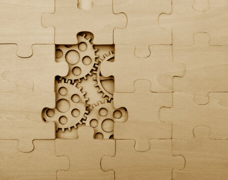 4 four interlocking wooden gears placed within a missing section of a large wooden jigsaw puzzle Human brain idea concept