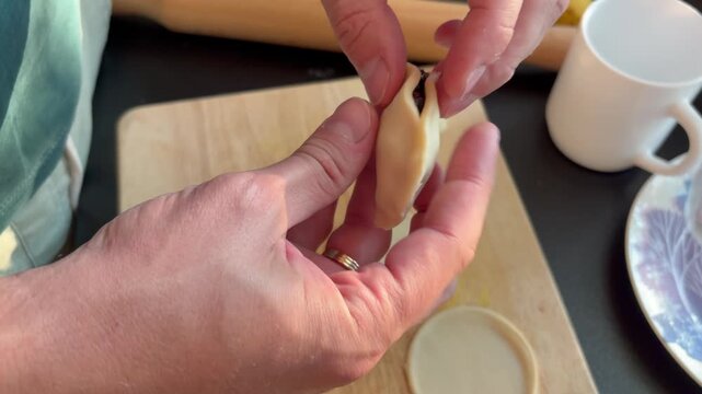 Man's hands shaping and sealing a dumpling with berry filling on a wooden board
