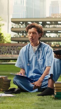 Vertical video: Medical students discuss coursework with a laptop and materials, seated on beanbags beside books and notes in a sunny campus courtyard during peer tutoring and outdoor group study.