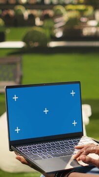 Vertical frame: The seated medical student holds a laptop with a blue screen on campus, providing an editable chroma key display for screen replacement in education content for medical school use.