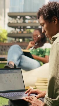 Vertical aspect: The student reviews renewable energy data on a laptop during campus study, with clean energy information and a blurred outdoor academic background.