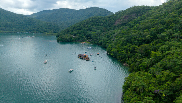 Aerial view of Saco do Ceu Restobar floating on the calm waters of Ilha Grande, surrounded by lush green hills and dense tropical forest in Rio de Janeiro, Rio de Janeiro, Brazil.