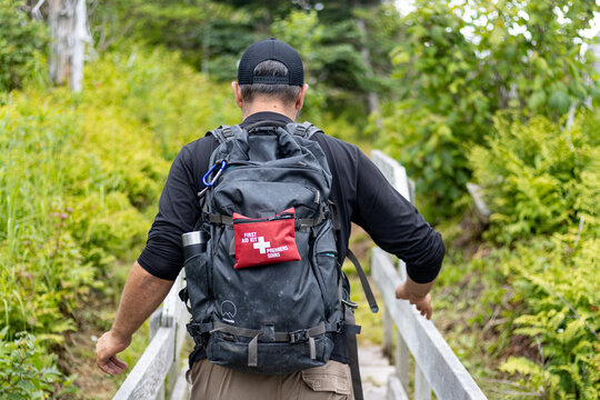 Gaspesie, Quebec, 15 July 2026 : A person wears a black backpack with a red first aid kit walking on a wooden path.