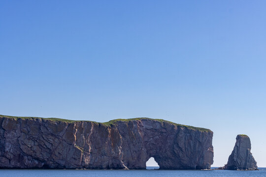 Gaspesie, Quebec, 15 July 2026 : A massive limestone rock formation with a natural arch and a sea stack rises from the ocean.