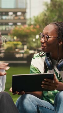 Vertical video: Women students discuss notes with a tablet while seated on campus beanbags, highlighting shared study session and project discussion, during peer tutoring, during group study.