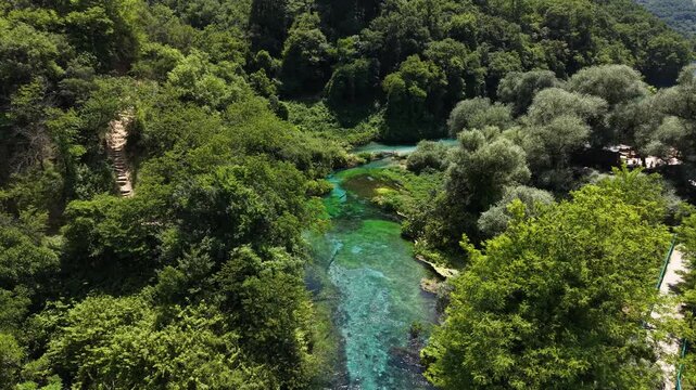 Aerial view of The Blue Eye natural spring with vibrant turquoise water surrounded by lush green forest and dense vegetation in Saranda, Qarku i Vlores, Albania.