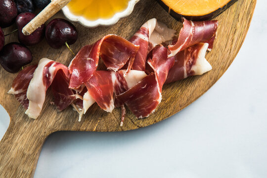Sliced jamon cheese, berry and honey on cutting board