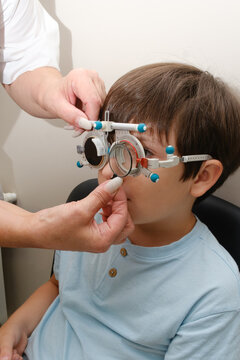 Optometrist adjusting trial frame glasses on boy during eye test in pediatric ophthalmology clinic for vision checkup.