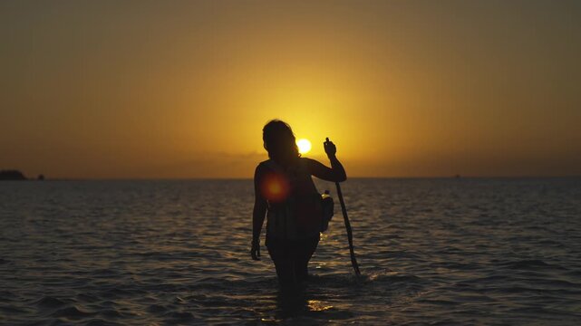 Woman walking through shallow water toward the sunset in Holbox, Mexico, slow motion