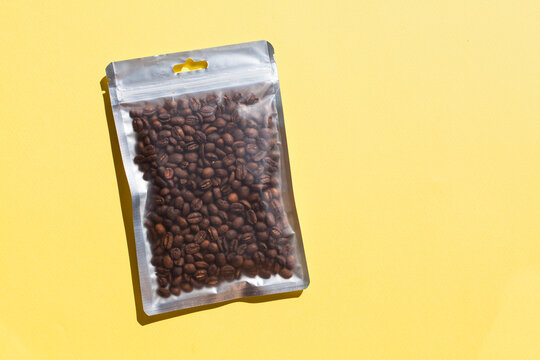 Blank craft plastic pouch mock up with coffee beans inside, transparent pack on studio background with shadow, mylar bag isolated for coffee product