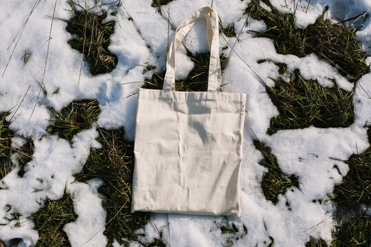 White cotton mesh bag on spring snow, green grass thawed patches background. Zero waste, no plastic, eco friendly shopping, recycling concept. Blank mockup shopper, place for text. copy space flat lay