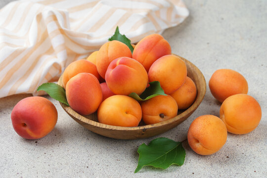 Fresh ripe apricots in rustic wooden bowl with green leaves on stone gray background. Healthy seasonal summer fruit, healthy food, natural nutrition, ingredient for cooking and desserts.
