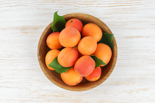 Fresh ripe apricots in rustic wooden bowl with green leaves on white wooden background. Healthy seasonal summer fruit, healthy food, natural nutrition, ingredient for cooking and desserts.