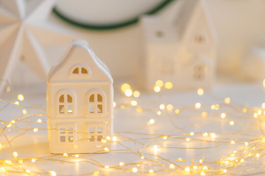 Soft Christmas scene with white ceramic house, glowing warm fairy lights and neutral winter decor. Cozy minimalist holiday background perfect for seasonal designs.
