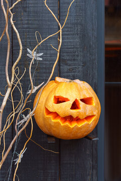 Glowing carved jack o lantern pumpkin on black wooden porch with natural branches. Classic Halloween holiday decoration creating a spooky autumn atmosphere, seasonal home decor.