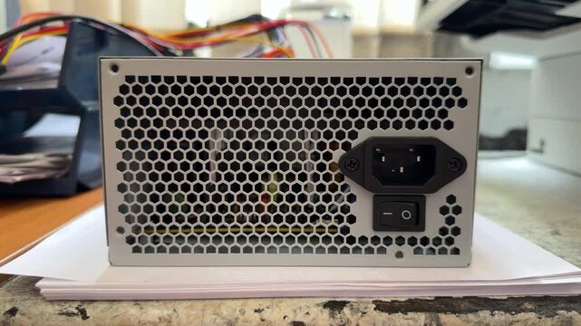 Computer power supply unit with ventilation grille and switch on workbench. Electronics repair, spare parts, hardware maintenance, workshop service