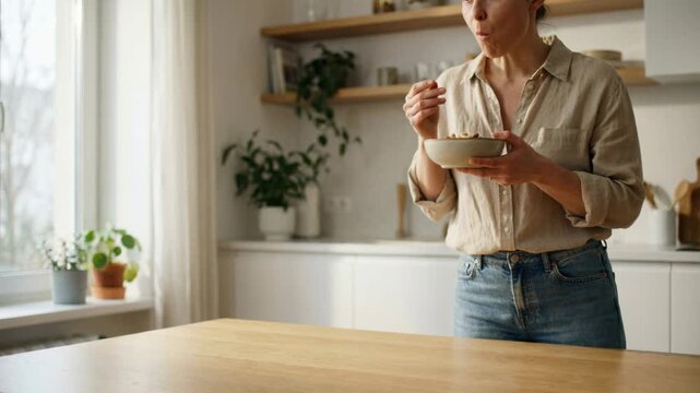 Woman holding and eating healthy snack at kitchen counter. Mindful eating and balanced diet for home healthcare.