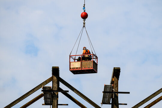 Construction workers in arial work basket over old tall wooden railroad trestle, train tracks removed, structural framework update, sunny summer day, America
