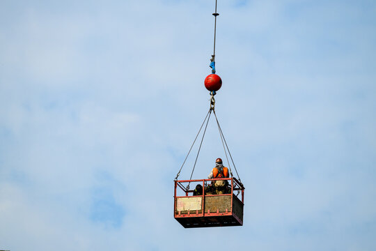 Construction workers in safety gear in arial work basket high up against a sunny blue sky, summer work project in America
