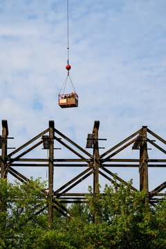 Construction workers in arial work basket over old tall wooden railroad trestle, train tracks removed, structural framework update, sunny summer day, America
