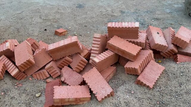 Pile of red ceramic bricks scattered on sandy ground at construction site. Building materials, house construction, masonry work, renovation supplies