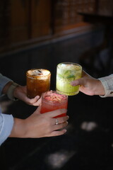 Two people toasting with colorful layered cocktails in dimly lit bar setting © vivi