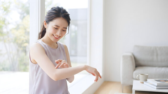 明るいリビングで腕の肌触りを確かめながら微笑む女性のボディケア