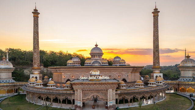 Aerial view of Mosque Samin Baitul Muttaqin with intricate golden domes, tall minarets, and ornate architecture illuminated by the warm sunset in Bojonegoro, East Java, Indonesia.