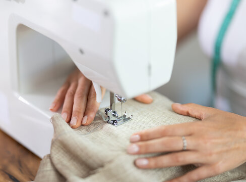 In workshop, female employee hand at work with sewing machine, close up. Worker sews clothes and participates in creation of fashionable clothing items from natural fabrics