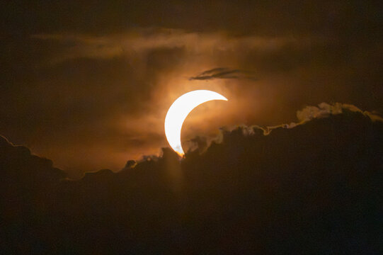 Aerial view of a partial solar eclipse partially obscured by dark clouds in the sky over Lugano, Ticino, Switzerland.