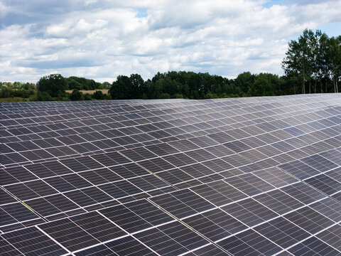 Aerial view of a large solar farm with rows of photovoltaic panels under a cloudy sky in Kaunas, Kaunas County, Lithuania.