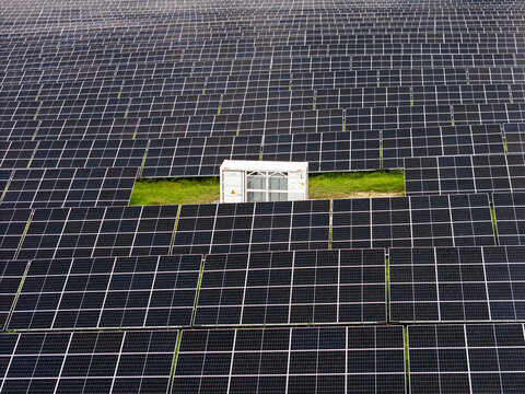 Aerial view of a large solar farm with rows of photovoltaic panels and a central electrical inverter station in Kaunas, Kaunas County, Lithuania.