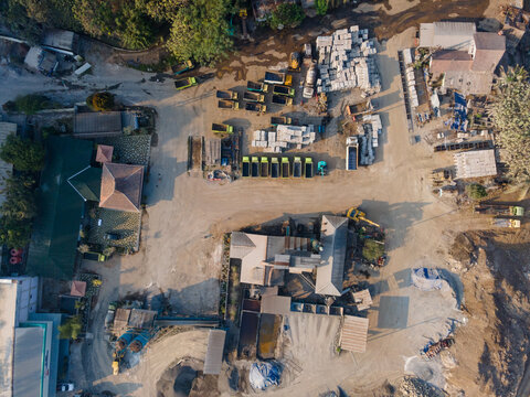Aerial view of a stone processing facility with trucks, piles of construction materials, and industrial buildings in Banyumas Regency, Central Java, Indonesia.