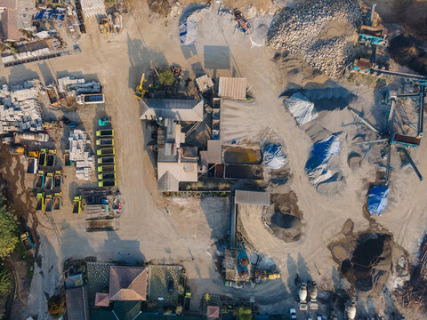 Aerial view of an industrial stone quarry and processing plant featuring piles of gravel, sand, heavy machinery, and trucks on a dusty site in Banyumas Regency, Central Java, Indonesia.
