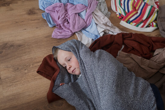  Little Girl Wrapped in a Blanket Lying on the Floor Among Clothes