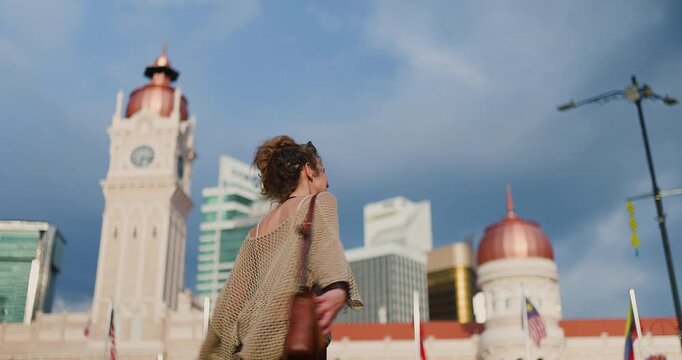 A joyful young woman, with a radiant smile, playfully strolls and poses before the majestic Sultan Abdul Samad Building in Kuala Lumpur, blending historical architecture with the vibrant modern city.