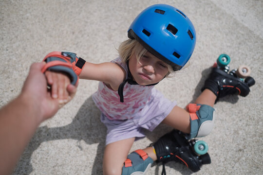 Little Girl Taking Helping Hand While Sitting on Roller Skates at a Skatepark