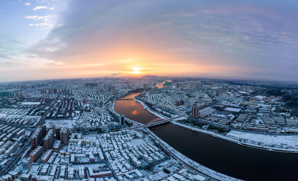 Aerial view of a snow-dusted urban city with a winding river at sunrise, casting warm light over the landscape.