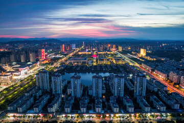 Fototapeta premium A twilight cityscape with illuminated buildings, a lake, and busy roads stretching across a modern urban district.