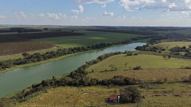 Aerial view of a winding river flowing through lush green agricultural fields and rolling hills under a blue sky with clouds