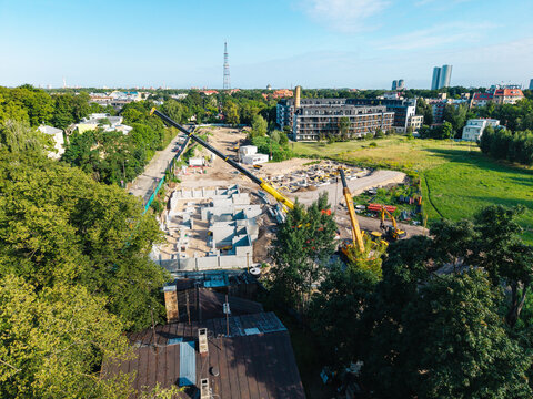 Aerial view of a construction site at 4A Cieceres Street in Agenskalns, featuring cranes and concrete foundations surrounded by trees and urban buildings in Riga, Latvia.
