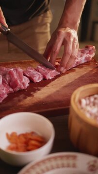 Close-up of a hand holding a pork rib cleaver on a wooden cutting board.