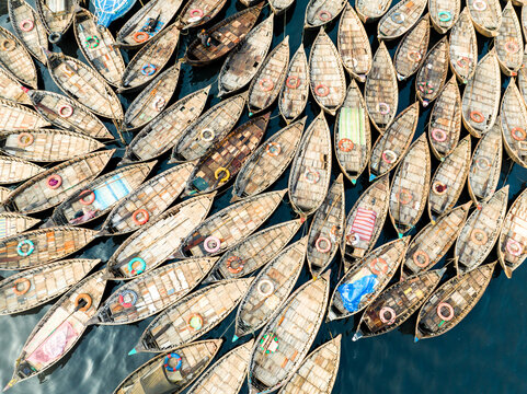 Aerial view of Sadarghat featuring numerous wooden boats docked closely together on the river, with colorful lifebuoys and textured wooden decks in Dhaka, Dhaka Division, Bangladesh.