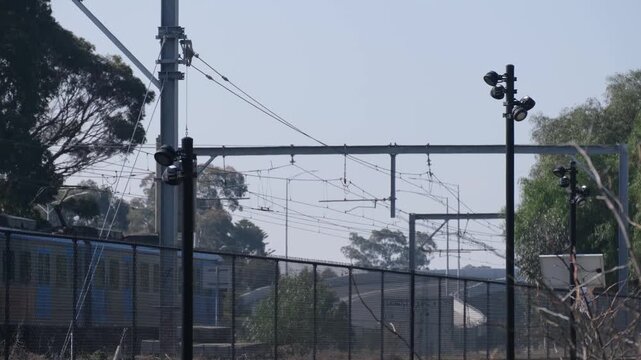 Overhead catenary wiring, steel gantries along Werribee Line as a train moves past behind security fencing&nbsp;in Melbourne Australia. Public rail transit, suburban transport networks